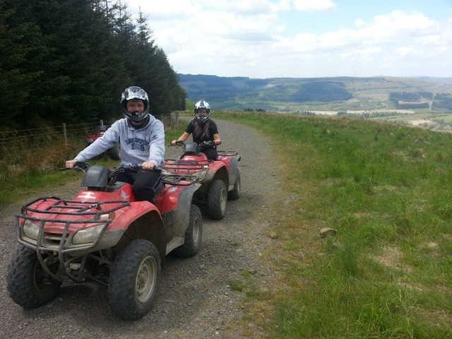  Dos niños con cascos blancos, sonriendo y a punto de conducir quads rojos alrededor del bosque 