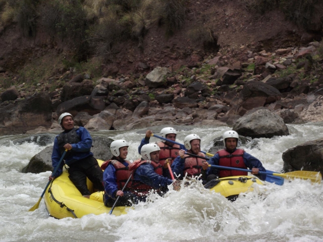 People wearing white helmet and red buoyancy aids doing rafting race