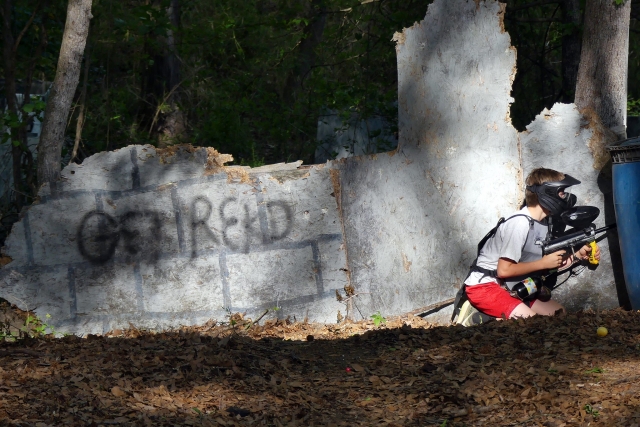 Kid wearing grey t-shirt and red shorts playing paintball