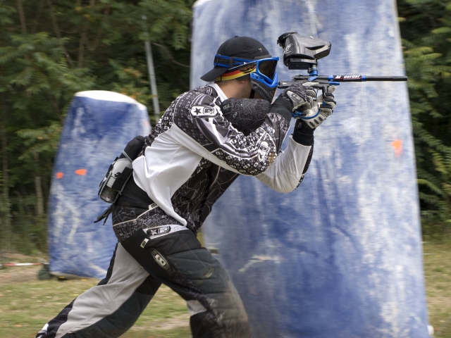 Young boy wearing mask and protective suit running while playing paintball
