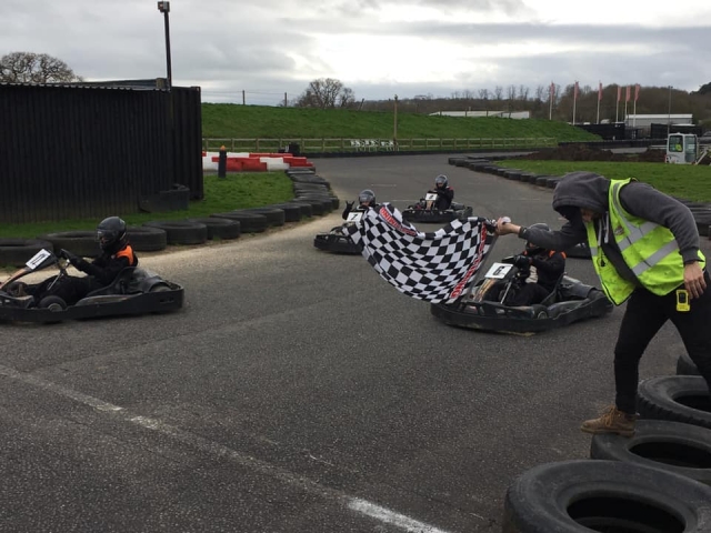 5 people wearing black helmets and driving suits during a karting race