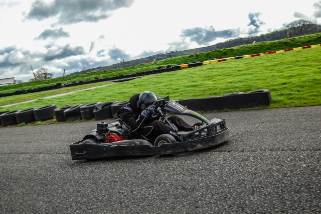 Driver wearing black helmet and driving suit karting