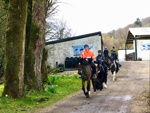  instructor con casco negro y chaqueta de naranja con niños paseando a caballo a caballo que pasean por los niños.
