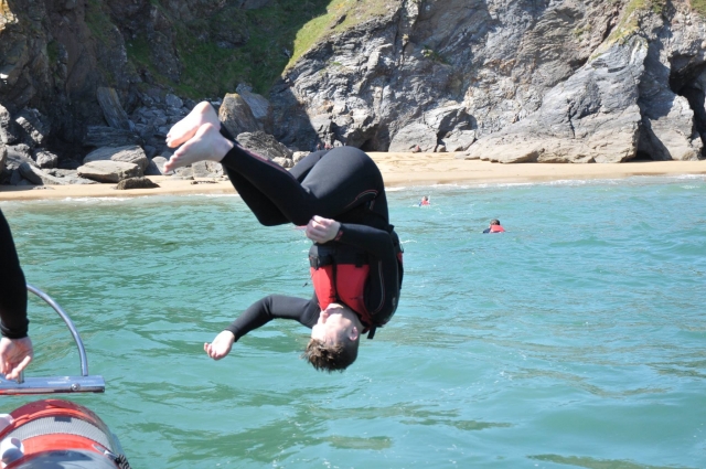 Boy wearing red buoyancy aids and black wetsuit jumping from a cliff