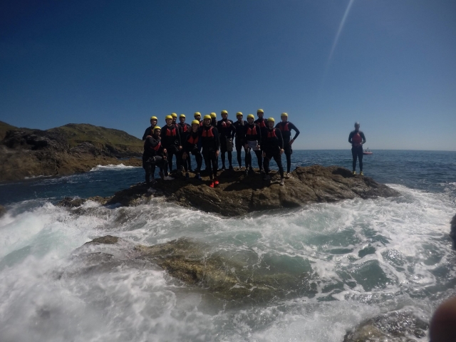  Gruppe von Freunden mit gelben Helmen und orangefarbenen Schwimmhilfen beim Coasteering 