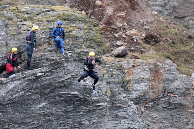 Menschen mit gelben Helmen und schwarzen Schwimmhilfen springen von der Klippe 