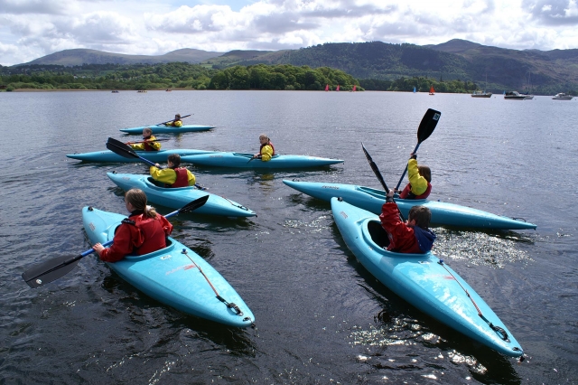  6 enfants portant des aides à la flottabilité rouges et jaunes faisant du kayak sur le lac 