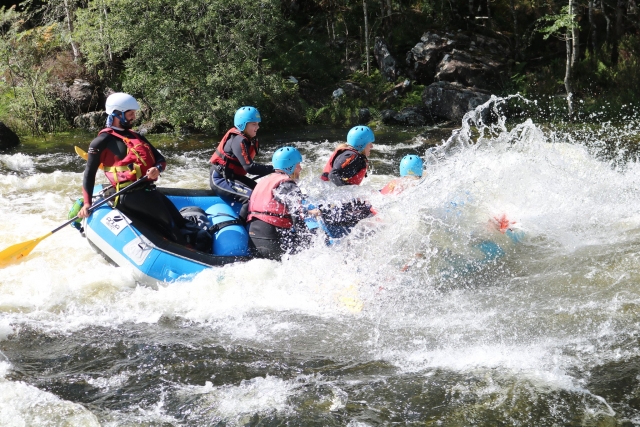 Persone che indossano ausili al galleggiamento rossi e caschi blu sono stati colpiti da un'onda sul fiume durante il rafting