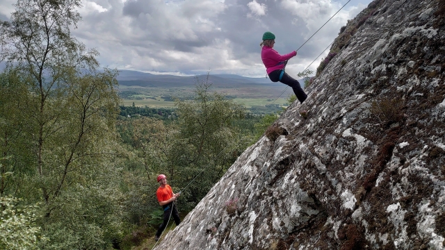  Donna con maglione rosa e casco verde e uomo che indossa casco rosso e t-shirt arancione da arrampicata