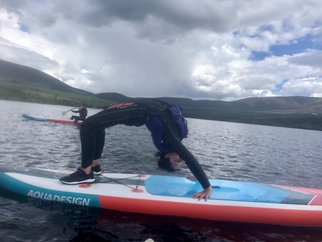  Ragazza che fa yoga, che indossa aiuti di galleggiamento blu durante la sua sessione di paddleboarding