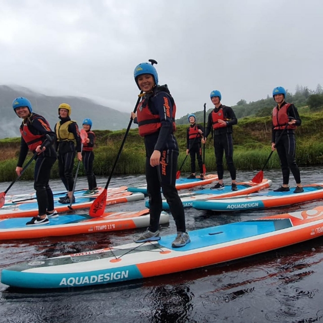  Persone che indossano caschi blu e aiuti di galleggiamento rossi che sorridono durante la loro esperienza di paddleboarding 