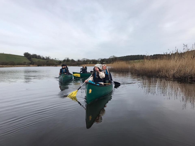  Ragazze con aiuti al galleggiamento neri su canoe verdi che fanno canoa tandem al lago