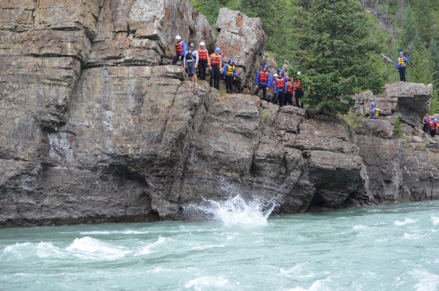  Grande gruppo di persone che indossano abiti rossi il galleggiamento aiuta a nuotare e saltare durante la loro avventura di coasteering