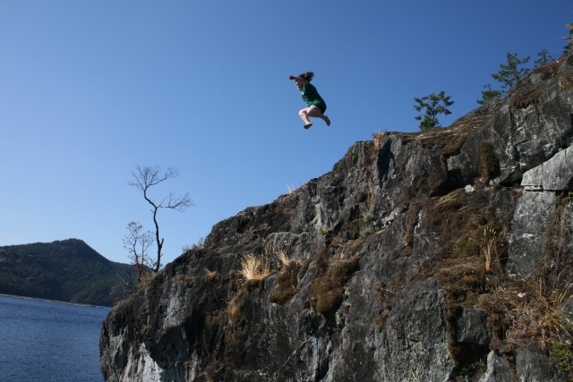  Ragazza con una maglietta verde che salta dalla scogliera durante il coasteering 