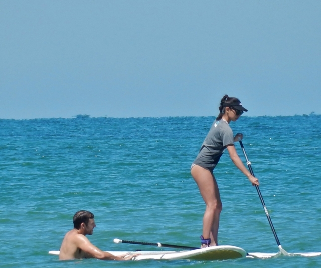 Girl in t-shirt and blue cap getting helped by her instructor during her paddleboarding experience 