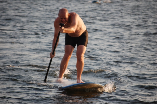 Man in black swimming suit smiling while paddleboarding