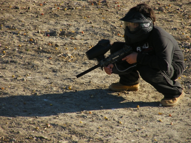 Ragazzo che indossa una maglietta nera, jeans e maschere che gioca a paintball 
