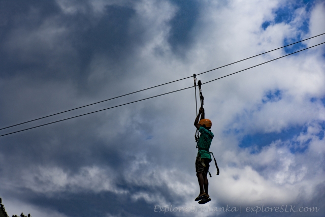 Boy wearing green t-shirt and orange helmet in the air while his zip-lining session