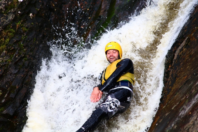 e-19759609-man-smiling-wearing-yellow-helmet-and-buoyancy-aids-jumping-from-a-waterfall16436133311882.jpg