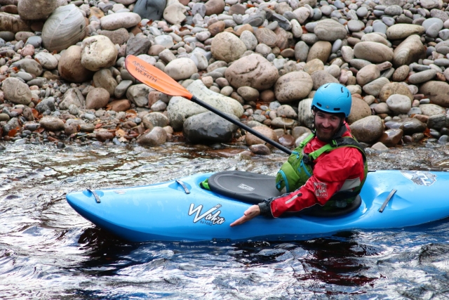 Man wearing blue helmet and green buoyanya ids kayaking