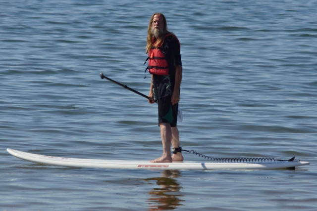  Mann mit langen Haaren und roten Schwimmhilfen beim Paddleboarding auf weißem Paddleboard 