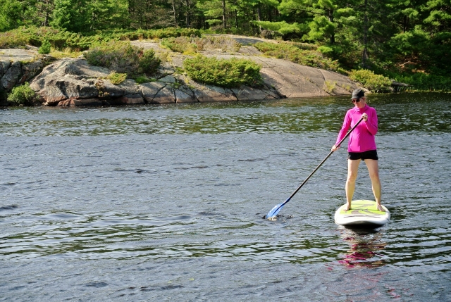  Frau mit pinkfarbener Jacke und Paddelmütze auf weißem Paddleboard