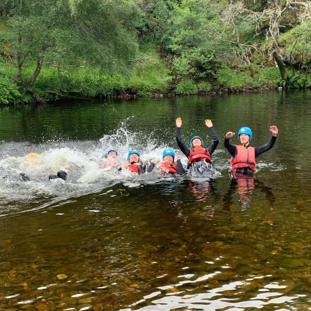  Freunde tragen rote Schwimmweste Kletterhilfen und blaue Helme, die während ihrer Canyoning-Session die Welle machen 