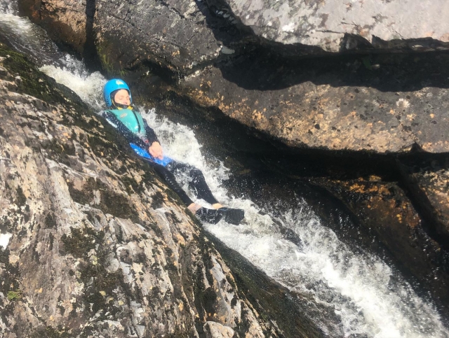  Mädchen mit blauem Helm und blauen Schwimmhilfen, das während ihrer Canyoning-Session vom Wasserfall springt 