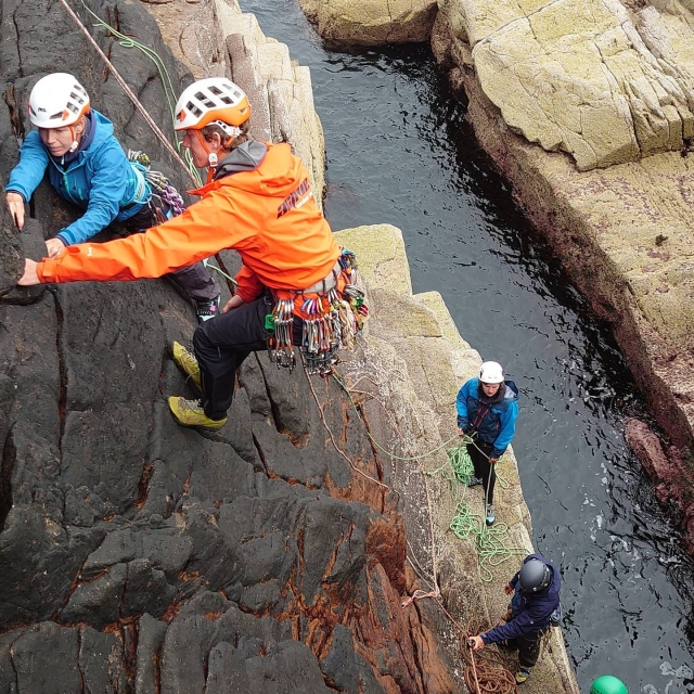  Menschen, die blaue Jacken und weiße Helme tragen, die im Rahmen ihrer Canyoning-Session klettern