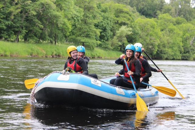  5 Personen mit roten Schwimmhilfen und blauen Helmen beim Rafting 