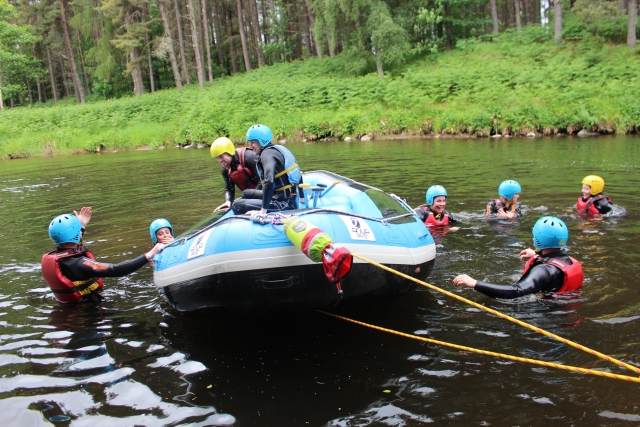  Menschen mit gelben und blauen Helmen und roten Schwimmhilfen schwimmen beim Versuch, auf das Brett zu steigen, um ihre Rafting-Session fortzusetzen 