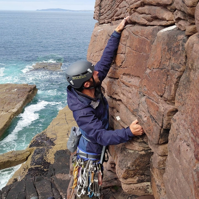  Junge mit schwarzem Helm und blauer Jacke klettern und das Meer im Hintergrund 