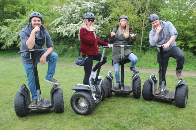 To girls and two boys wearing grey helmets and striking a pose before going to segway around the park