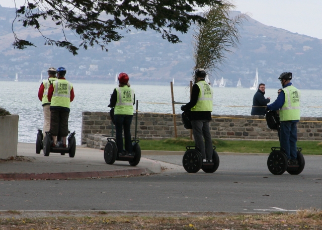 Four people wearing black helmets doing segway around the park