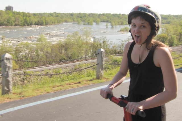 Girl wearing black helmet, black t-shirt and showing the tongue while she enjoys segway