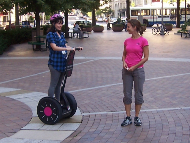 Girl wearing pink helmet, smiling and getting the briefing by her instructor, who is wearing pink t-shirt. She is getting ready to do a segway session