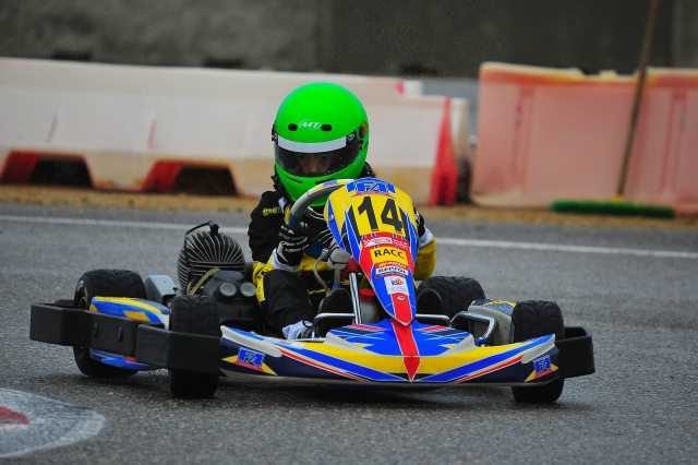 Boy wearing green helmet and driving blue karting