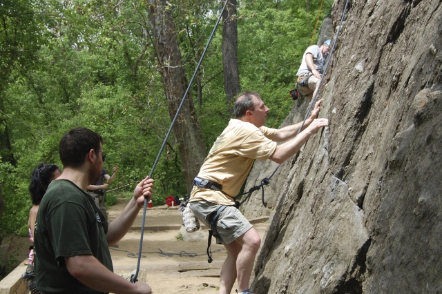 Man in yellow t-shirt getting ready for rock climbing with the help of his family and the instructor