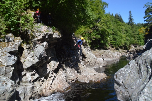 Kid wearing yellow helmet and blue buoyancy aids jumping from a cliff