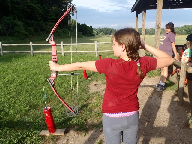  Fille en t-shirt rouge avec sa mère derrière elle pratiquant le tir à l'arc pour la première fois 