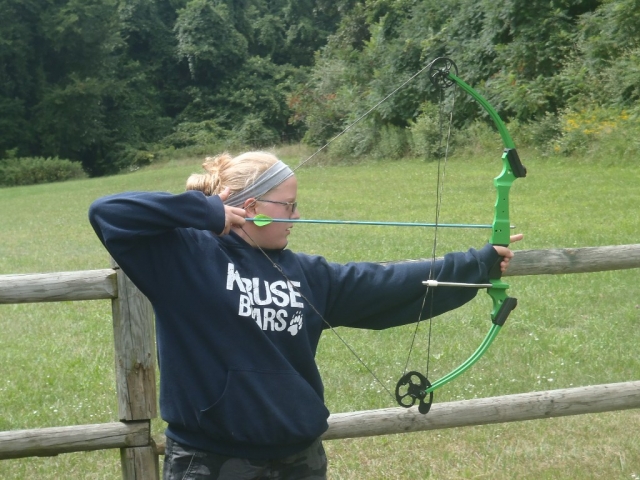  Fille blonde en pull noir s'amusant avec le tir à l'arc pour la première fois 