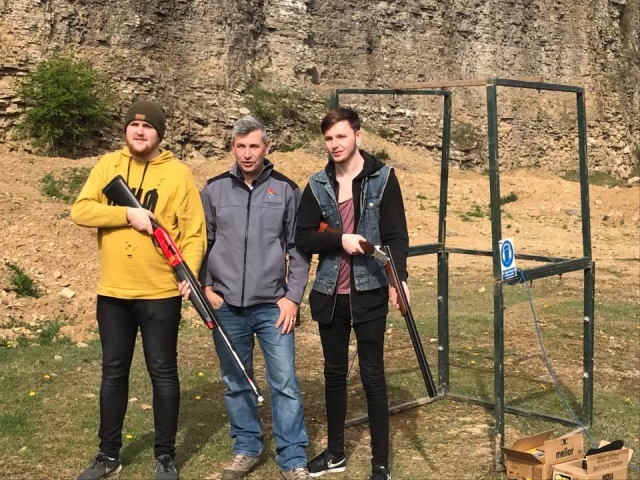 Two boys, one wearing black jacket and the other yellow jacket and green hat, about to start their clay pigeon shooting with the instructor