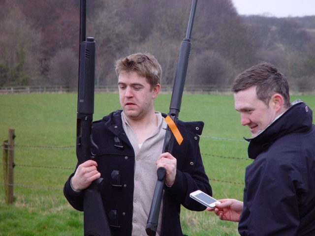Two young boys wearing black jackets loading the guns to shoot them