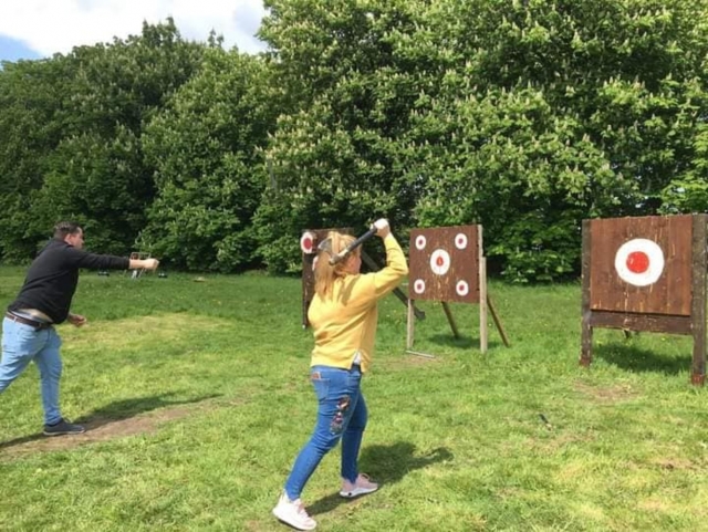 Young blond girl in yellow sweater axe throwing
