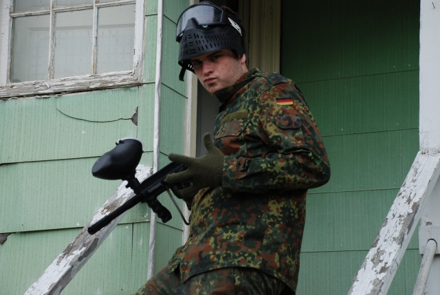  garoto usando terno de camuflagem e máscara preta prestes a jogar paintball
