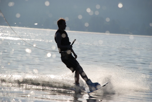Menino vestindo auxílios negros de flutuabilidade e fazendo wakeboard 