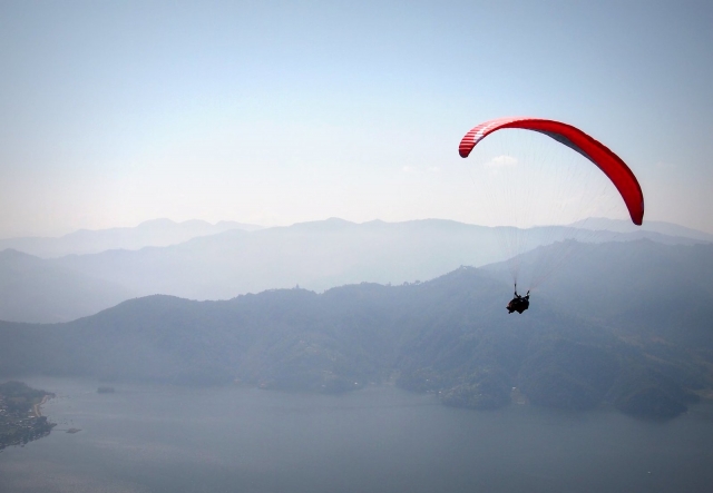 Person enjoying the view from a red flying paraglider
