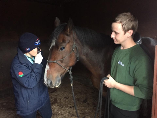 Homem de camiseta verde e garoto de suéter preto cuidando de um cavalo antes de sair para seu passeio 