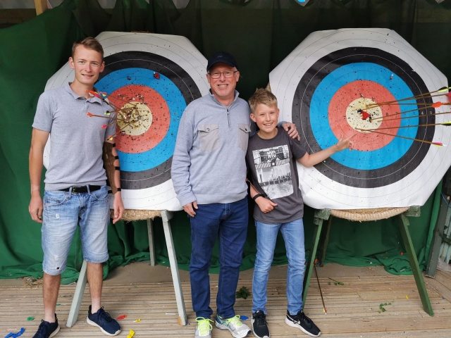  Padre e hijo sonriendo al lado de su instructor durante su sesión de tiro con arco 