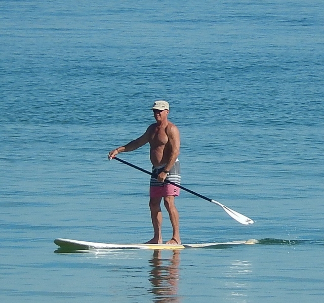 Man wearing pink swimming suit, white cap and paddleboarding